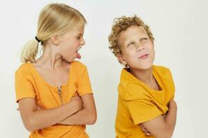 two joyful children in yellow t-shirts standing side by side childhood emotions light background unaltered photo