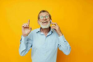 Photo of retired old man talking on the phone posing close-up yellow background