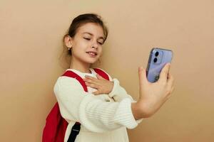 Portrait of happy smiling child girl with phone posing red backpack isolated background photo