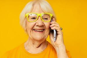 sonriente mayor mujer hablando en el teléfono en amarillo lentes aislado antecedentes foto