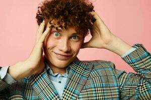 Young curly-haired man gesturing with his hands emotions checkered jacket pink background unaltered photo