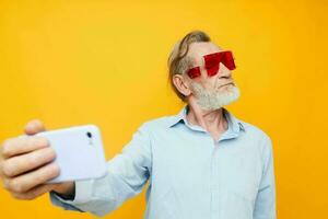 Cheerful elderly man in fashionable glasses with telephone yellow background photo