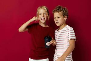 boy and girl are standing next to a disposable glass with a drink red background photo