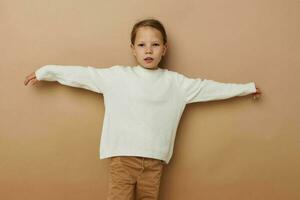 Portrait of happy smiling child girl in white sweater posing hand gestures beige background photo