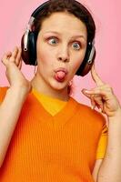 cheerful woman listening to music with headphones orange sweater emotions fun isolated backgrounds unaltered photo