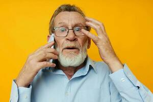 Photo of retired old man talking on the phone posing close-up yellow background