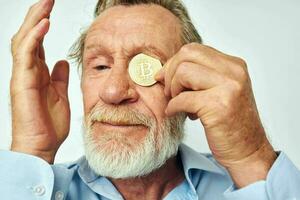 Senior grey-haired man finance gold coins bitcoin near face light background photo