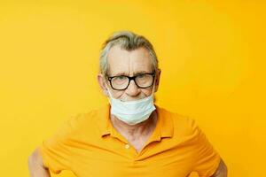 Senior grey-haired man medical mask on the face protection close-up yellow background photo