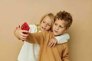 Photo of two children in sweaters posing for fun with phone isolated background