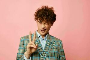 Young curly-haired man gesturing with his hands emotions checkered jacket pink background unaltered photo