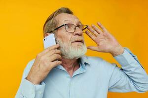 Senior grey-haired man talking on the phone posing close-up yellow background photo