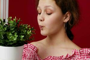 attractive young woman in pink blouse is posing with a plant in white pot photo