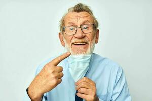 retrato de contento mayor hombre en camisa con Corbata médico máscara la seguridad ligero antecedentes foto