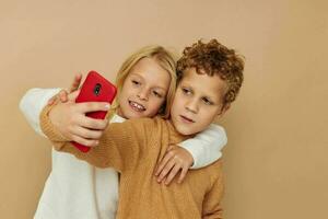 Photo of two children in sweaters posing for fun with phone isolated background