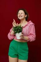 cheerful woman holding a pot with a flower in her hands red background photo