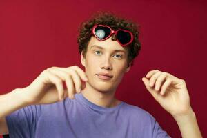 Young curly-haired man hand gestures heart shaped glasses posing isolated background photo