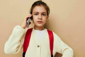 Portrait of happy smiling child girl talking on the phone with a backpack beige background photo