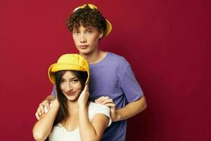 young man and girl in colorful t-shirts stylish clothes hats red background photo