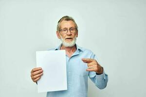 retrato de contento mayor hombre participación un sábana de papel espacio de copia posando aislado antecedentes foto