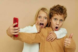 Photo of two children in sweaters posing for fun with phone isolated background