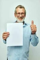 Senior grey-haired man in a blue shirt and glasses a white sheet of paper cropped view photo