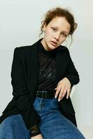 alegre mujer sentado en un silla en un negro chaqueta Moda posando ligero antecedentes inalterado foto