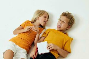 picture of positive boy and girl lie on the floor with notepads and pencils isolated background unaltered photo