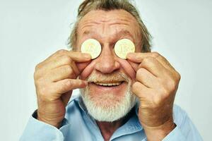 Senior grey-haired man in a blue shirt bitcoins on the face isolated background photo