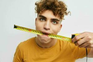 Attractive man measuring tape measure in yellow t-shirt light background photo