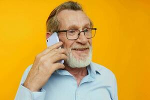 Portrait of happy senior man gray beard with glasses talking on the phone yellow background photo