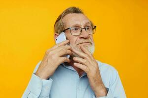 Photo of retired old man gray beard with glasses talking on the phone yellow background