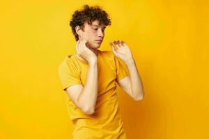 Young curly-haired man yellow t-shirt fashion hand gestures isolated background unaltered photo