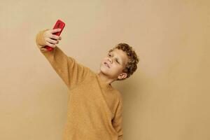 alegre chico con rojo teléfono en manos posando beige antecedentes foto