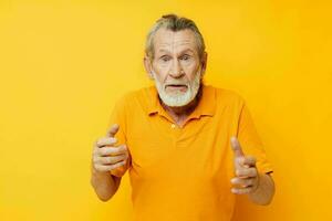 Senior grey-haired man with a gray beard emotion gestures hands yellow background photo