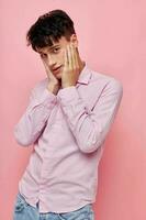 A young man in a pink shirt gesturing with his hands pink background unaltered photo