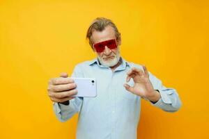 Portrait elderly man in fashionable red glasses with a phone isolated background photo