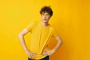 portrait of a young curly man wearing stylish glasses yellow t-shirt posing yellow background unaltered photo