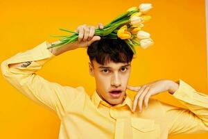 Photo of romantic young boyfriend with a bouquet of flowers posing a gift yellow background unaltered