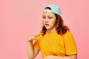 beautiful woman in a yellow t-shirt and blue cap posing emotions pink background unaltered photo