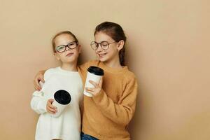 two little funny girls a glass with a drink beige background photo