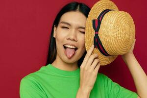 Portrait Asian beautiful young woman gestures with his hands with a hat in a green t-shirt red background unaltered photo