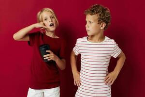 boy and girl are standing next to a disposable glass with a drink red background photo