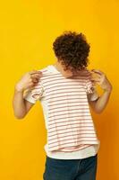 guy with red curly hair in a white t-shirt holds a striped t-shirt fashion youth style yellow background unaltered photo