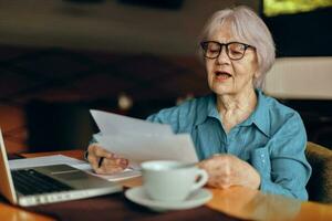 retrato de un mayor mujer sentado en un café con un taza de café y un ordenador portátil persona de libre dedicación trabajos inalterado foto