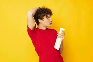 cute red-haired guy in a red t-shirt detergents in hands posing yellow background unaltered photo