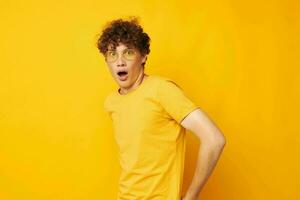 Young curly-haired man yellow t-shirt glasses fashion hand gestures isolated background unaltered photo