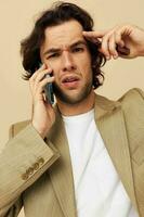 alegre hombre en un traje posando emociones hablando en el teléfono beige antecedentes foto