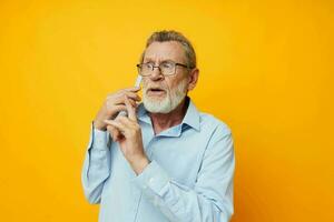 foto de retirado antiguo hombre en un azul camisa y lentes hablando en el teléfono amarillo antecedentes