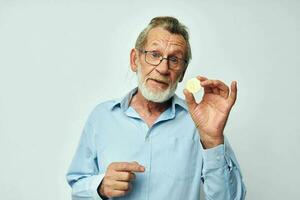 Photo of retired old man in blue shirts bitcoin in hands light background