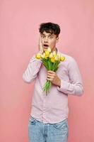 pretty man in a pink shirt with a bouquet of flowers gesturing with his hands pink background unaltered photo